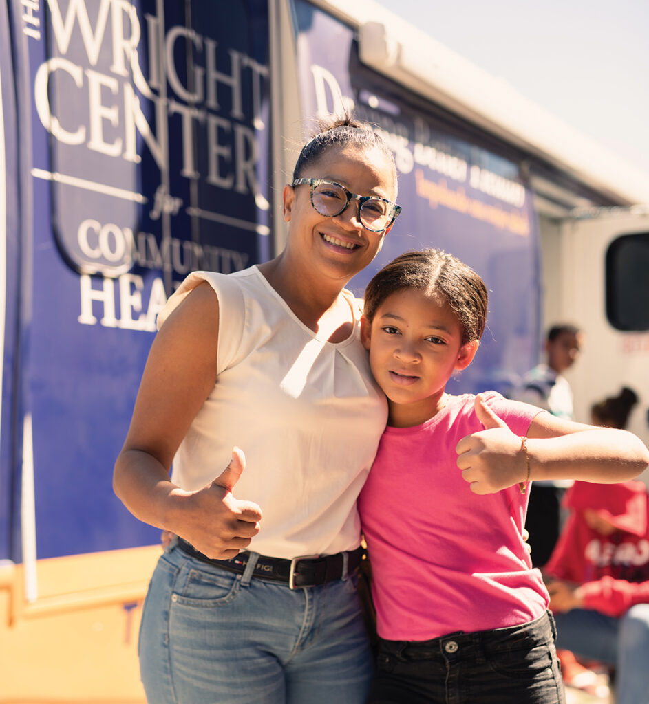 Mother and daughter pose for photo in front of Driving Better Health mobile medical vehicle