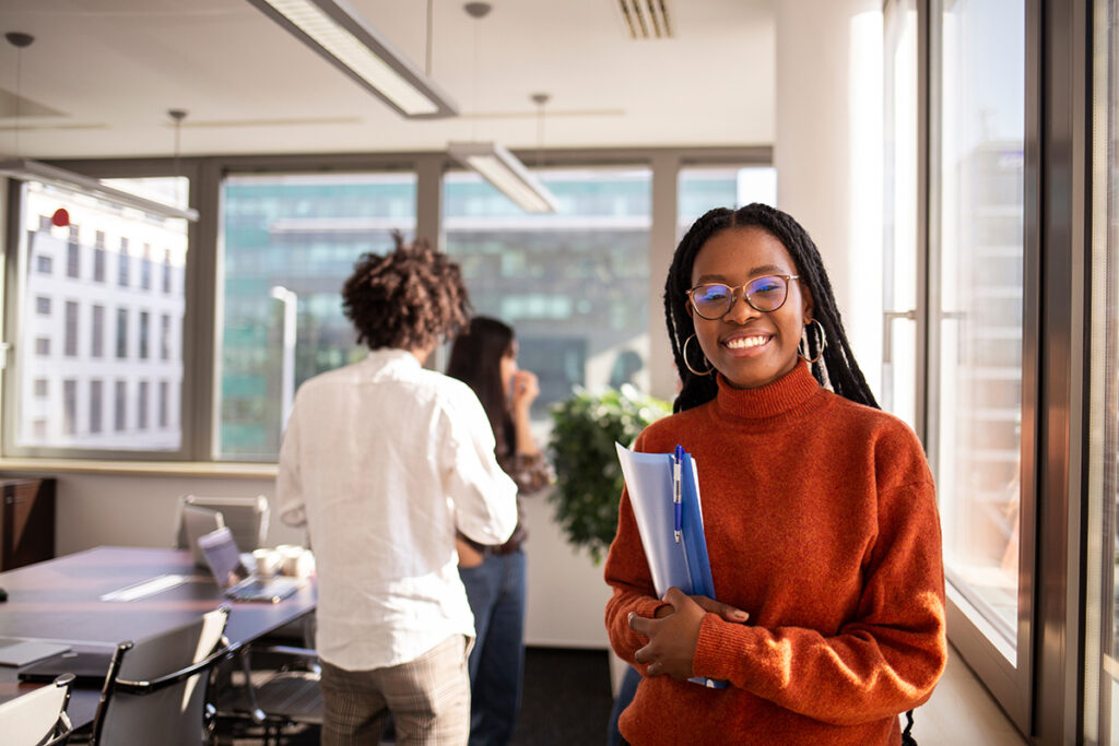 Female intern in office in foreground is looking at camera